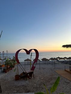 a heart shaped sculpture sitting on top of a sandy beach next to the ocean at sunset