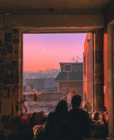 two people looking out an open window at the city below and pink sky in the distance