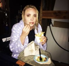 a woman sitting at a table eating food from a plate with fries in front of her