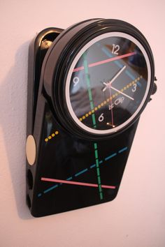 a black clock mounted to the side of a white wall with lines painted on it