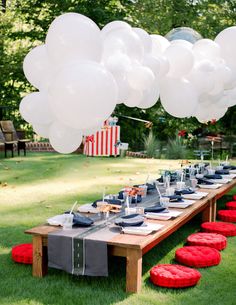 a long table with balloons and plates on it in the middle of an outdoor area