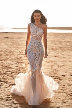 a woman standing on top of a sandy beach wearing a white and nude colored dress