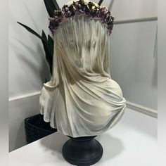 a white statue with purple flowers on it's head