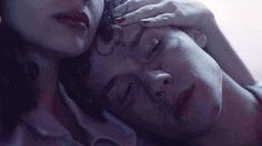 a man and woman laying next to each other with their eyes closed, one is holding her head