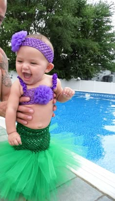 the baby is wearing a green and purple outfit with flowers on it's head