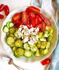 a white bowl filled with cucumbers, tomatoes and feta cheese next to a fork