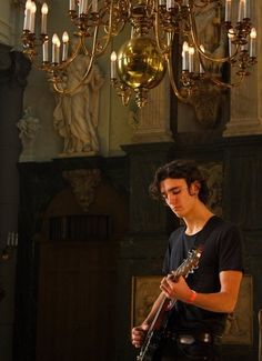 a young man playing an electric guitar in front of a chandelier with candles