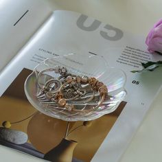 an open book with jewelry on it next to a pink rose and a vase filled with flowers