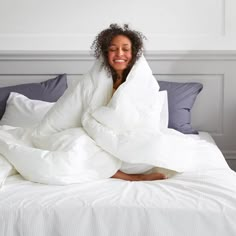 a woman wrapped up in a blanket on top of a bed with white sheets and pillows