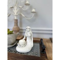 a white mermaid figurine sitting on top of a tray next to a potted plant