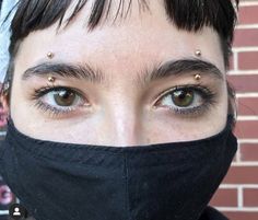 a close up of a person wearing a face mask with piercings on their eyes