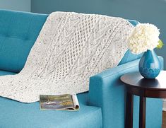 a blue couch with a white crocheted blanket on it and a vase with flowers