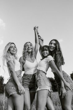 four women are standing in a field and one is holding her hand up to the sky