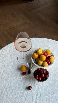 a glass of wine sitting on top of a table next to some cherries and oranges