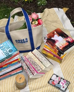 there is a tote bag, books and other items on the blanket outside with flowers