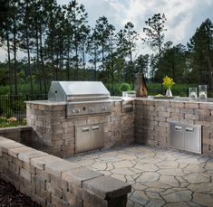 an outdoor kitchen with grills, sink and counter tops in the middle of a stone patio