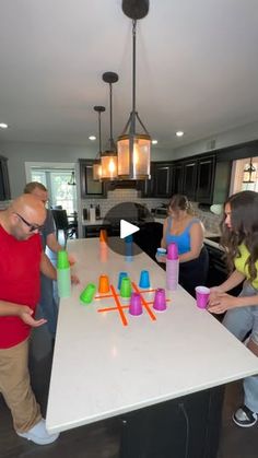 a group of people standing around a kitchen table with cups on it and one person pointing at them