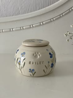 a white vase with blue flowers and the words bailey painted on it's side