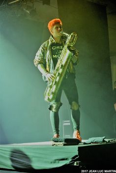 a man standing on top of a stage holding a large object in his hand and wearing green pants