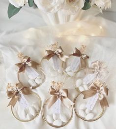 four wedding favors with ribbons and tags on them sitting on a white tablecloth next to flowers