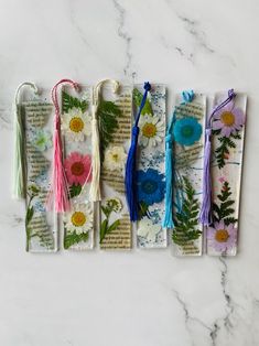 five bookmarks with flowers and tassels on them sitting on a marble surface