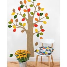 a tree with colorful leaves on it next to a chair and potted plant in front of the wall