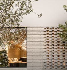 a white brick wall next to a tree and patio area with furniture on the other side