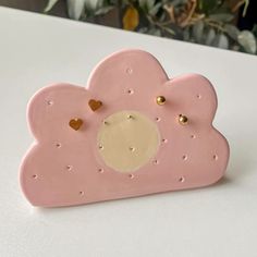 a pink cloud shaped clock with gold hearts on it's face and two holes in the middle