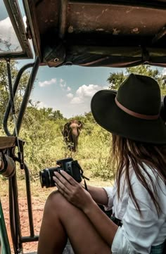 a woman sitting in the back of a vehicle with a camera on her lap and an elephant behind her