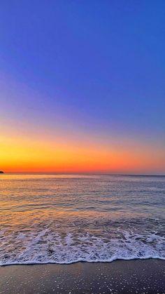 the sun is setting over the ocean with waves coming in to shore and an island in the distance