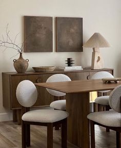 a dining room table with four chairs and a vase on the sideboard next to it