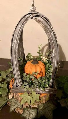 a pumpkin is sitting in a metal basket with greenery on the table next to it