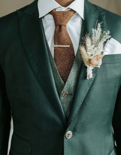 a man in a green suit with a brown tie and flower boutonniere