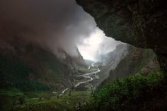 the view from inside a cave looking down at a river running through it and mountains in the distance