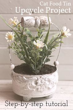 Cat food tin upcycle project with step-by-step tutorial. Rustic white tin with embossed flower and leaves with a wire and wood handle. A small faux daisy-like plant is in the tin along with faux dirt. Tin Upcycle, Tin Can Decorations, Decoupage Tins, Recycled Tin Cans, Tree Cottage, Tin Can Art, Aluminum Can Crafts, Recycle Cans, Altered Tins