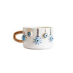 a white mug with blue eyeballs and gold rings on the handle is shown against a white background