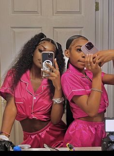 two women in pink outfits taking pictures with their cell phones