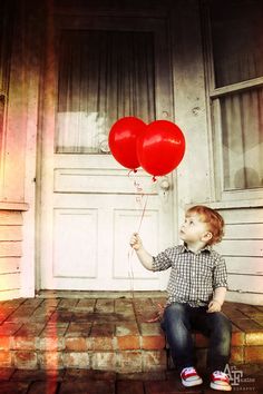 a little boy sitting on the steps holding two red balloons