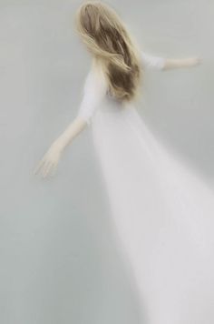 a blurry image of a woman in a white dress with her arms spread out