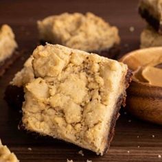 two pieces of brownie next to a wooden bowl with peanut butter in it on a table