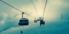 the ski lift is going down the snowy mountain with two people on it's back