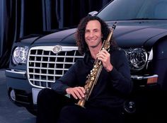 a man sitting in front of a car holding a saxophone