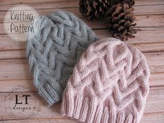 two knitted hats sitting on top of a wooden table next to a pine cone