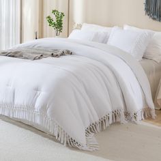 a bed with white linens and fringed edges is shown in front of a window