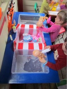 children are sitting at a table with toys in plastic containers on top of the table