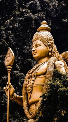 a statue of a person holding a spear and wearing a headdress with trees in the background