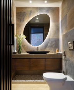 a bathroom with a round mirror above the sink and toilet in front of an open window