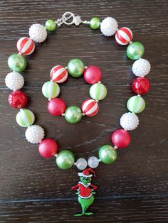 "How The Grinch Stole Christmas Inspired Children's Chunky Bubblegum Bead Necklace & Bracelet Set/ Holidays This very cute Christmas Grinch Necklace & Bracelet Set is a perfect addition to any holiday outfit and the holiday season. The Necklace is made up primarily of 20mm beads in shades of red, green and white. The necklace measures approximately 11\" when toggled around neck including the Grinch pendant. The Bracelet is an elastic bracelet, doubled up for extra strength. The Necklace Festive Christmas Beads With Round Shape, Festive Christmas Beads, Christmas Festive Round Beads, Christmas Holiday Necklace With Round Beads, Adjustable Christmas Festive Necklaces, Adjustable Festive Necklaces For Christmas, Adjustable Festive Necklace For Christmas, Adjustable Round Beads Necklaces For Christmas, Christmas Beaded Necklaces