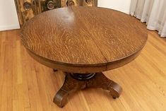 an old wooden table on a hard wood floor with white curtains in the back ground