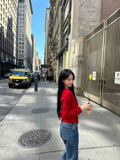 a woman is standing on the sidewalk and looking at her cell phone while holding something in her hand